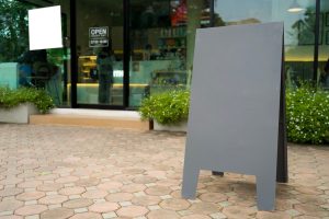 Empty black A-frame sandwich board placed on pavement in front of modern cafe